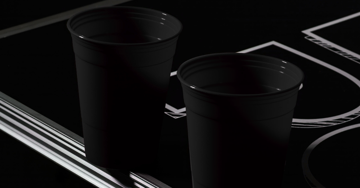 Zwei schwarze Beerpong Becher auf einem Bierpong Tisch stehend
