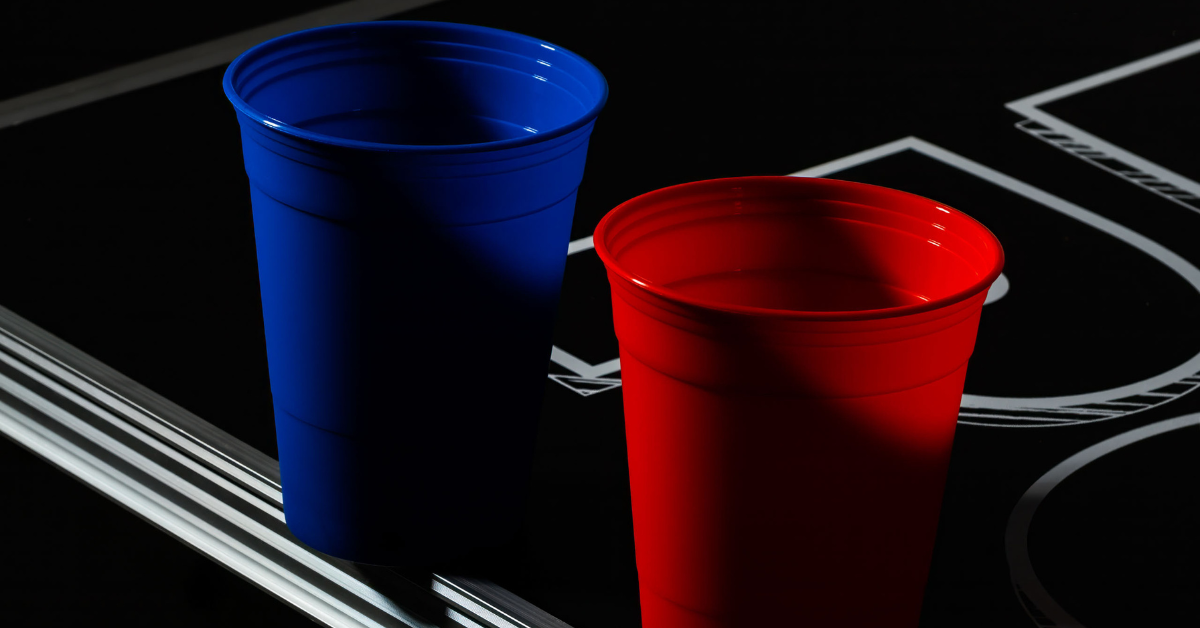 Ein einzelner roter und blauer Beerpong Becher auf einem Bierpong Tisch stehend